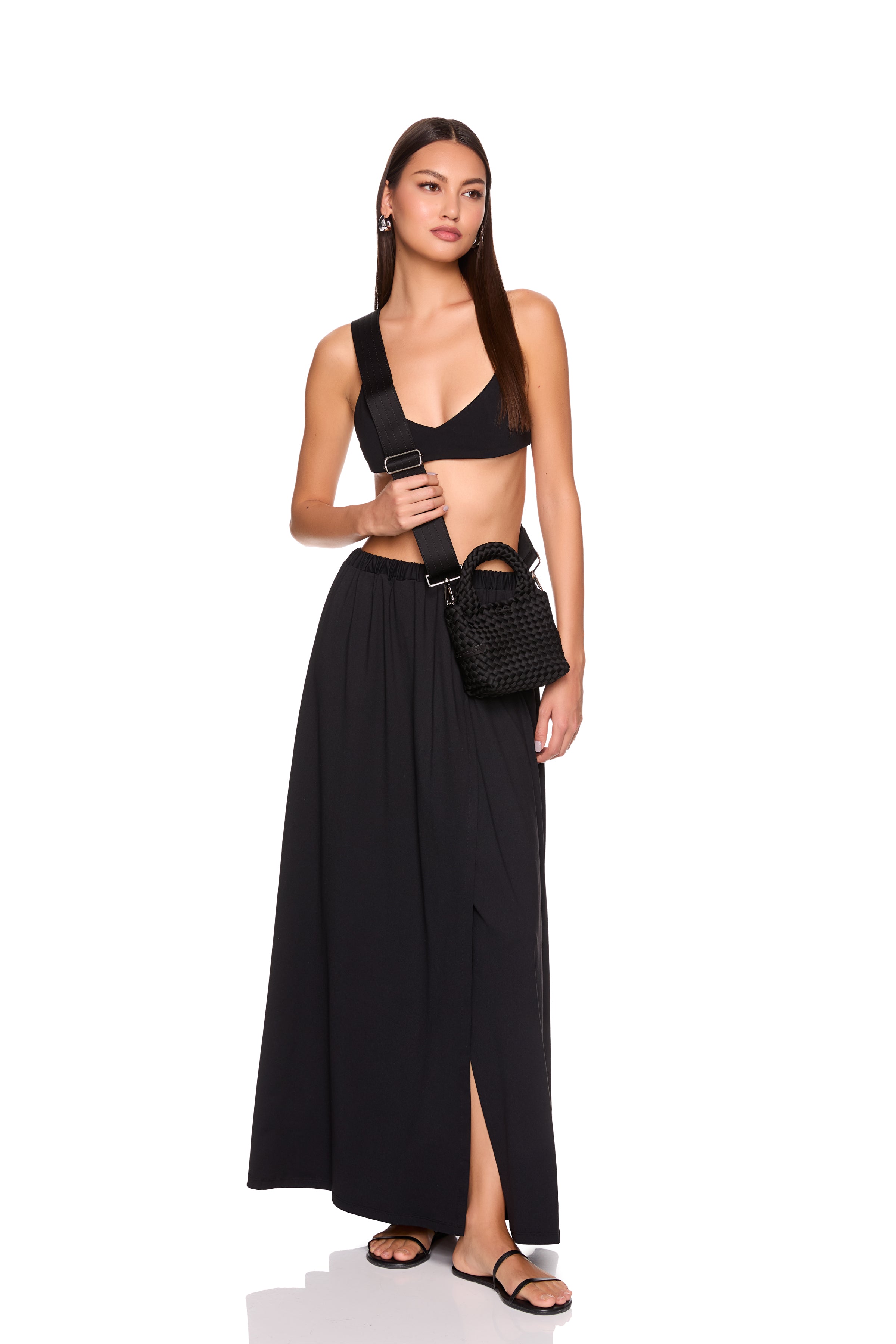 Woman wearing a black outfit with a belt and mini neoprene cross body bag bag on a white background