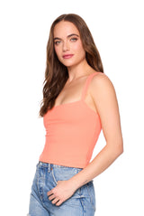 Woman wearing a peach-colored tank top and blue jeans on a white background