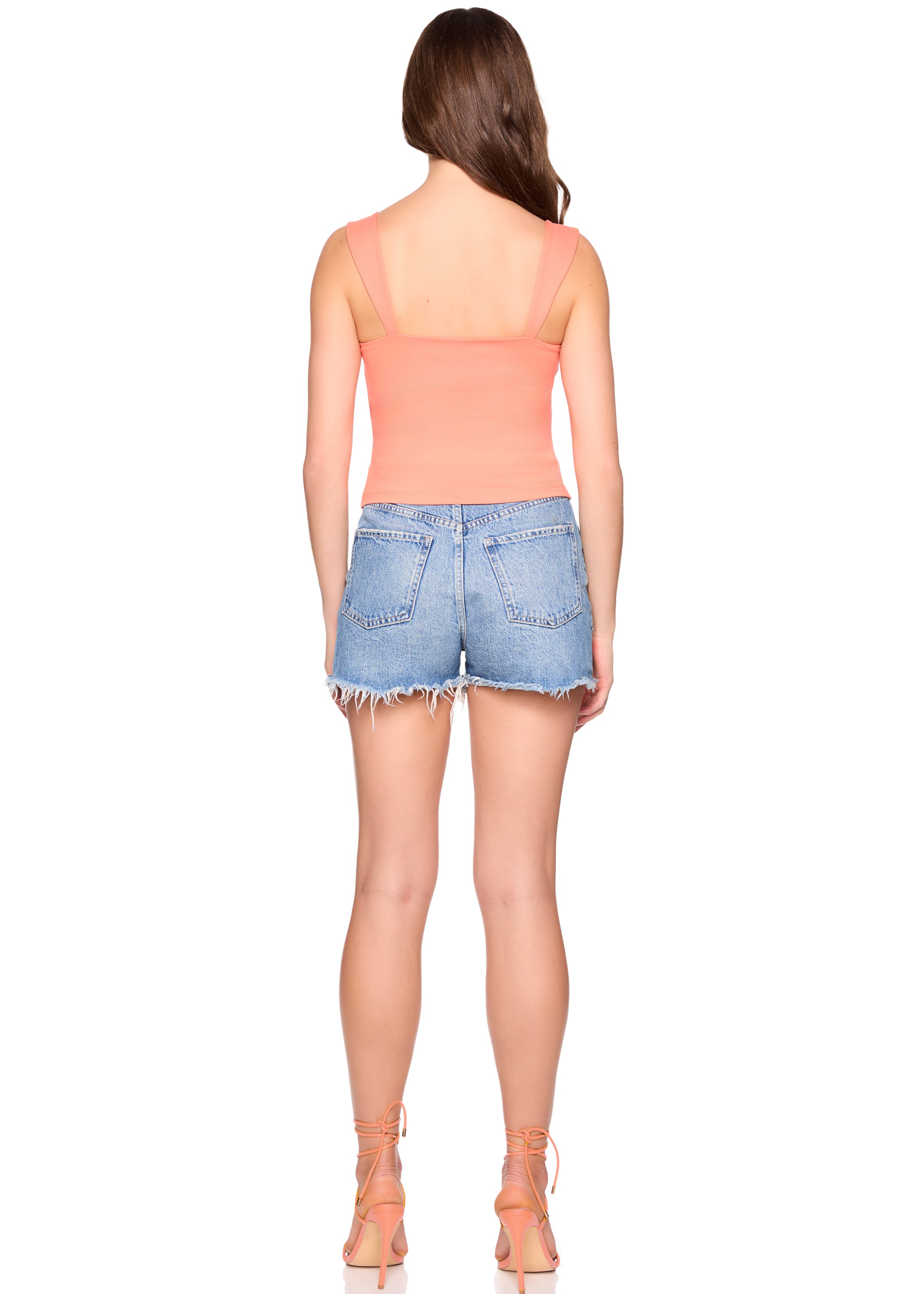 Woman wearing a peach strapless top and denim shorts on a white background