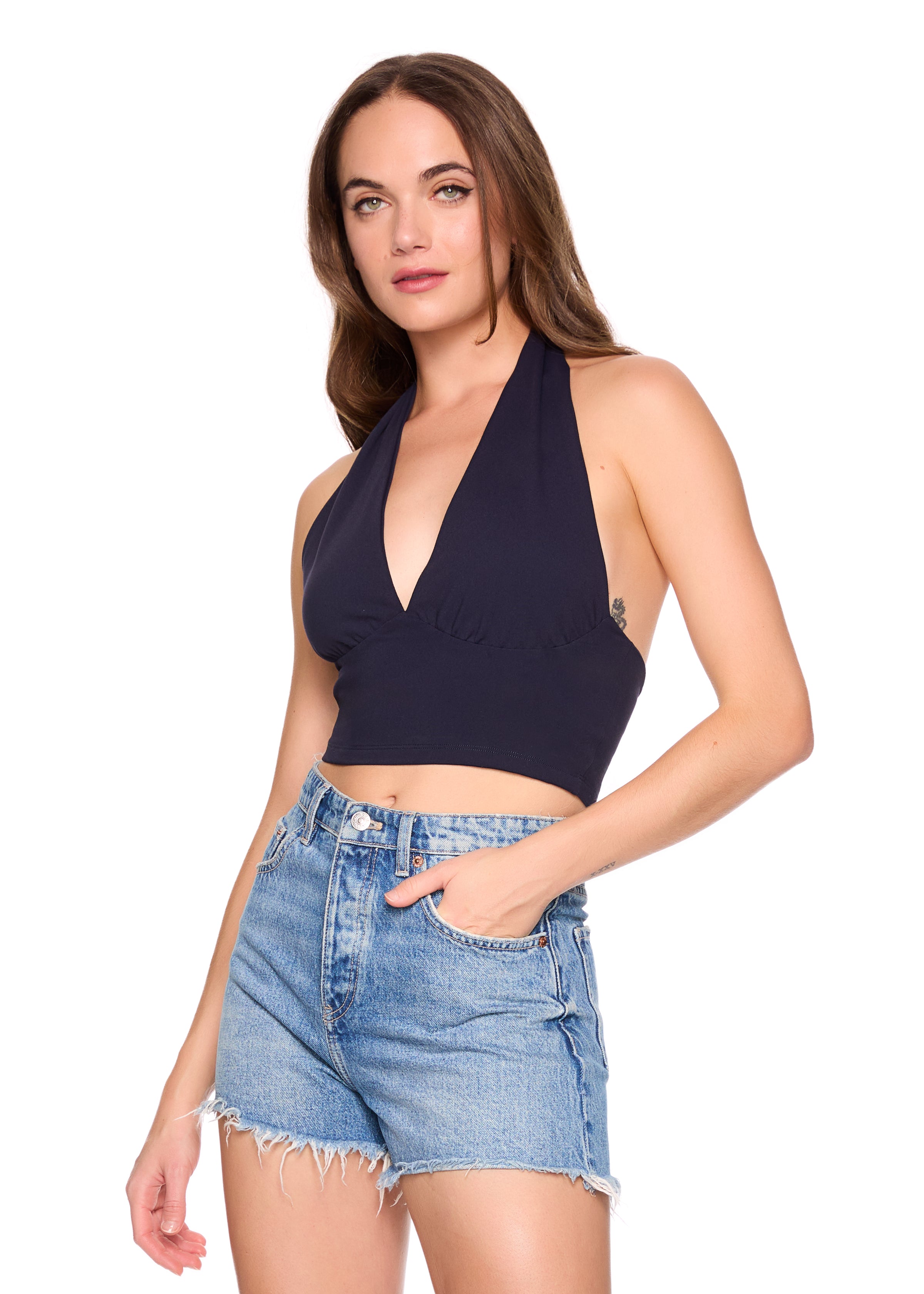 Woman wearing a navy halter top and denim shorts on a white background
