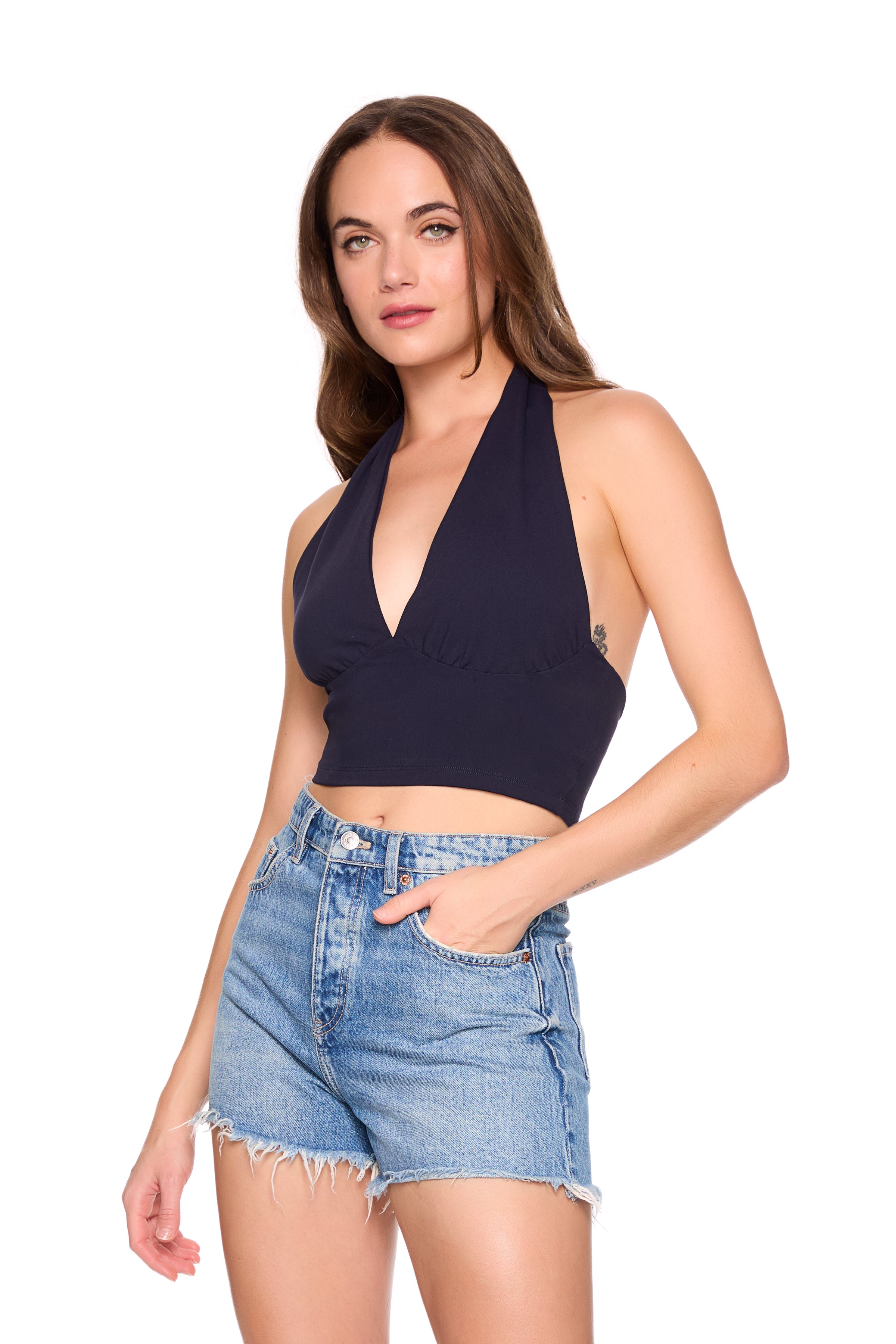 Woman wearing a navy halter top and denim shorts on a white background