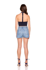 Woman wearing a navy halter top and denim shorts on a white background