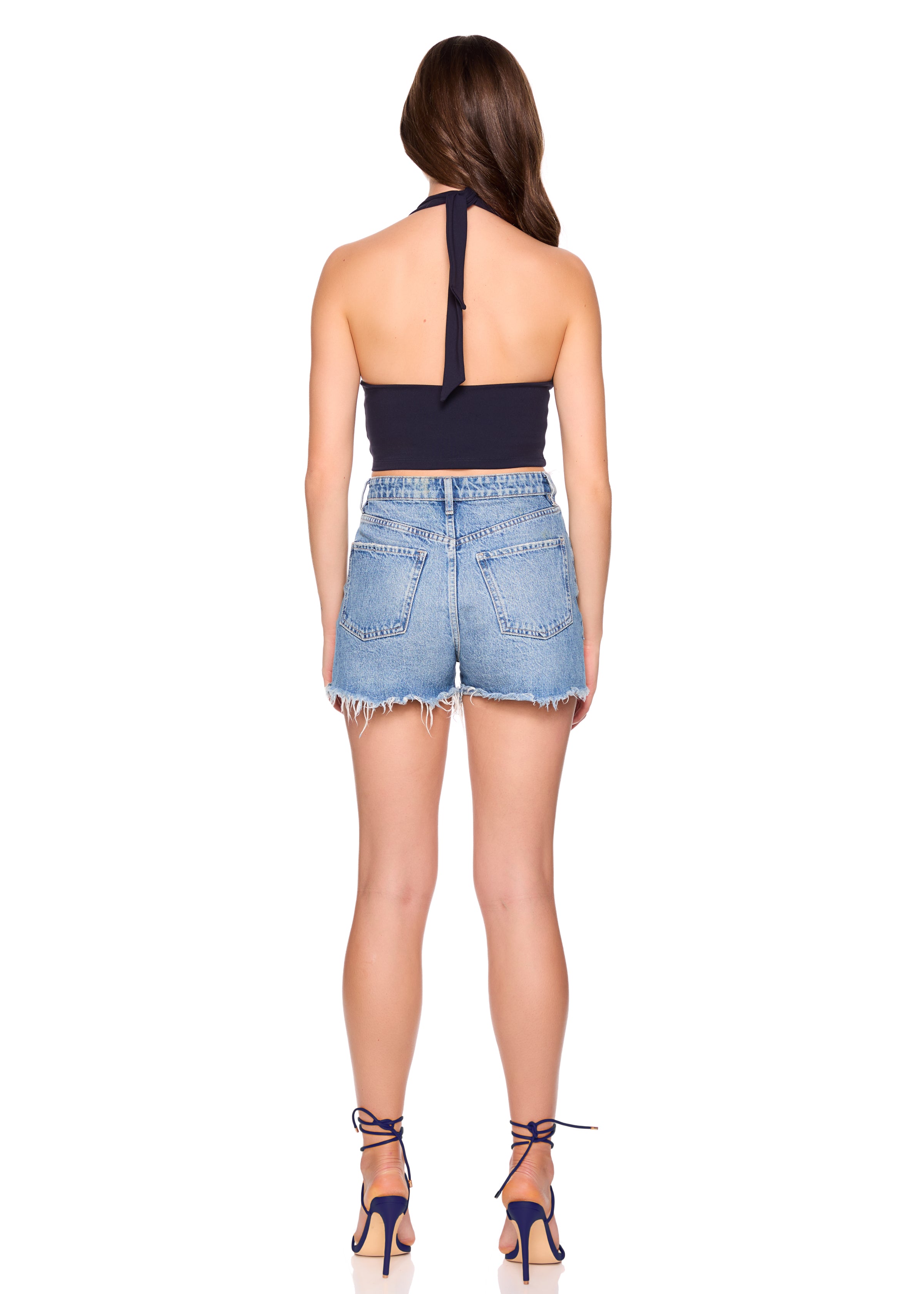 Woman wearing a navy halter top and denim shorts on a white background